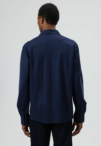 Marineblauw shirt met lange mouwen van gladde stof met een puntige kraag, geruite manchetten en een ontspannen pasvorm, met minimale stikseldetails.