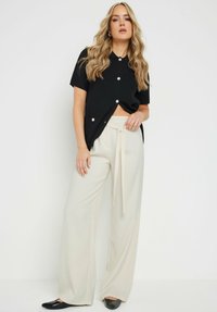 Camisa corta de manga corta negra con cierre de botones, combinada con pantalones de pierna ancha de cintura alta en color crema y bailarinas negras.