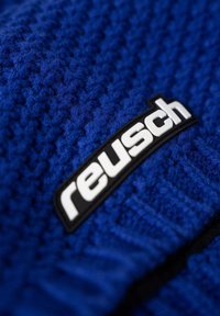 Blue knitted fabric, featuring a textured surface. A black patch displays the "reusch" logo in white, positioned prominently.