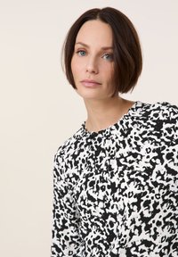 Schwarz-weiße Bluse mit einem abstrakten Leopardenmuster, runder Ausschnitt und weicher Textur.