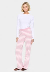 Witte langarmtop gecombineerd met roze-witte gestreepte pyjamabroeken met een brede tailleband en een losse pasvorm, gedragen met bruine Slippers.