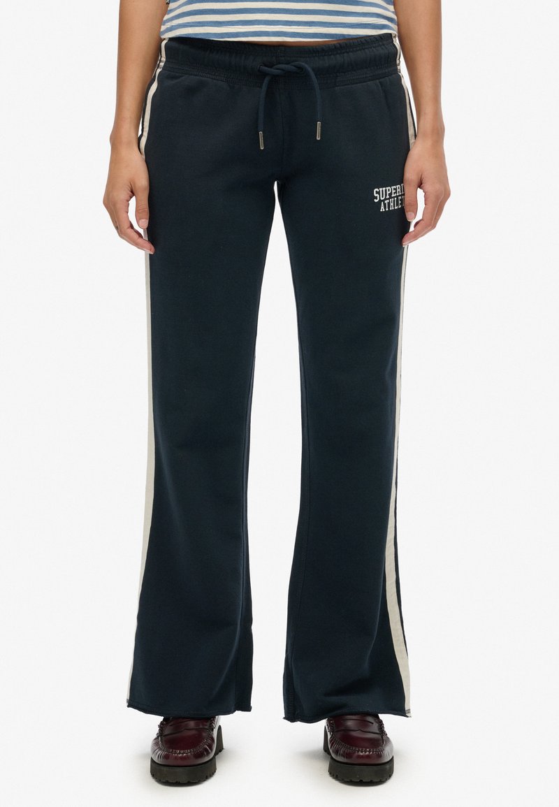 Marineblauwe sweatpants met crèmekleurige zijstrepens, voorzien van een elastische tailleband en trekkoord. Logo detail op de linker dij. Flare pijp ontwerp.