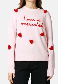 Maglione rosa lavorato a maglia con testo ricamato rosso "Love is overrated" e sei applicazioni a forma di cuore rosse sulle maniche e sul petto.