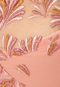 Tessuto rosa con ricami intricati che presentano motivi floreali in rosa chiaro, oro e fili di rosa più scuro, su uno sfondo texturizzato.