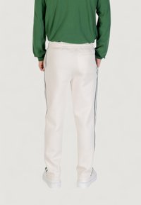 Weiße Sporthose mit schwarzen Seitenstreifen, elastischem Bund und einer Gesäßtasche, kombiniert mit einem grünen Langarmshirt.