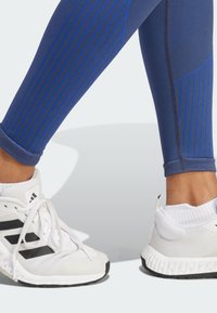 Niebieskie legginsy sportowe z pionowymi prążkami i dopasowanym krojem, zestawione z białymi sneakersami z czarnymi akcentami i teksturowanymi podeszwami.