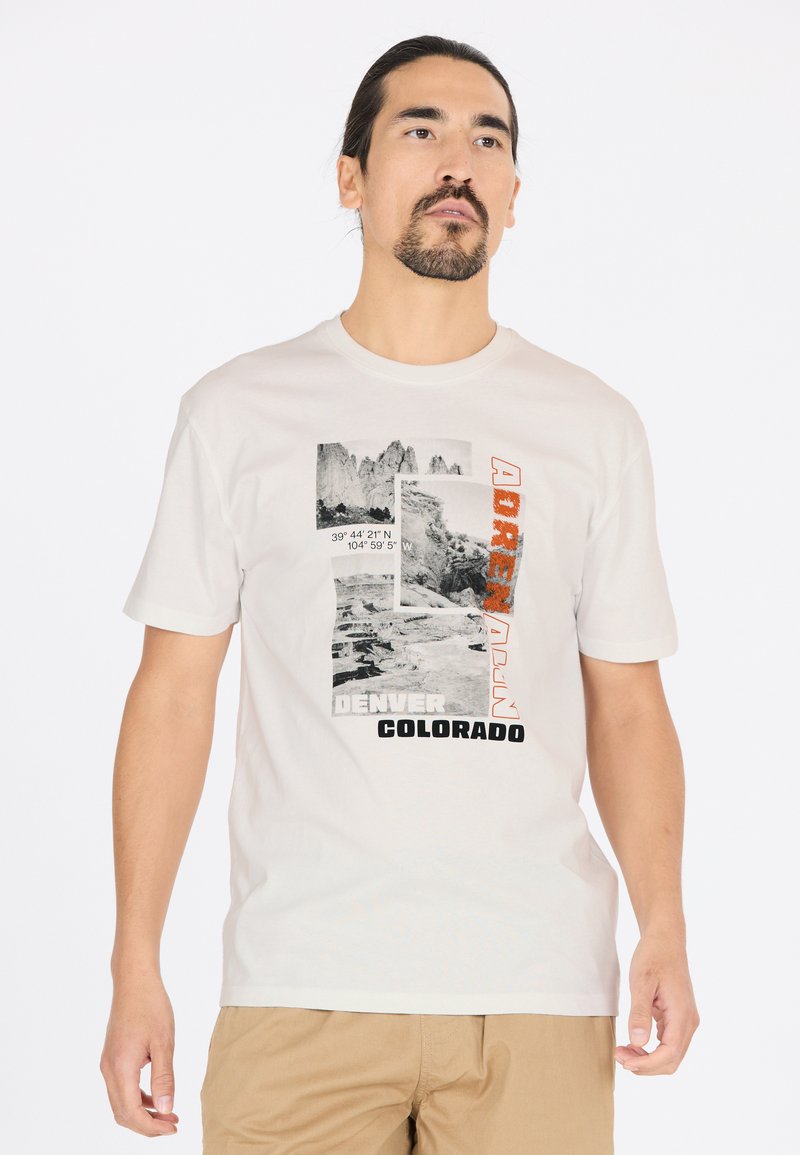 Ljust beige t-shirt med ett grafiskt motiv som har svart och orange text, bergbilder och geografiska koordinater. Kortärmad, rund hals.