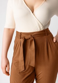 Cuerpo de punto acanalado en crema con un diseño cruzado, combinado con pantalones marrones de tiro alto que cuentan con un cinturón atado y pliegues. El conjunto muestra una textura suave.