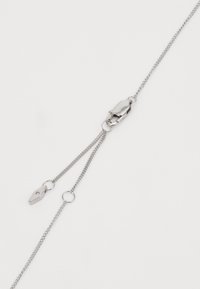 Sølvmetal kæde med to strenge, der har en muslingekrog og en spids charm. Glat tekstur, minimalistisk design og skinnende finish.