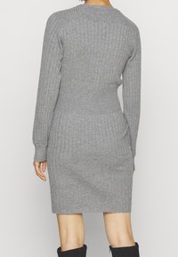 Harmaa ribbineulottu mekko, jossa on pitkät hihat, vartalonmyötäinen siluetti ja pyöreä pääntie. Pehmeä tekstuuri ja polvipituinen malli.