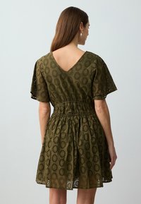 Olivgrünes Kleid aus strukturiertem Stoff mit floralem Lochmuster, featuring einem V-Ausschnitt auf der Rückseite, kurzen Ärmeln und einem elastischen Bund.