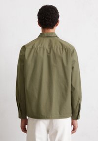 Groene, lichte shirt met een kraag, knoopmanchetten en een ontspannen pasvorm. De stof heeft een gladde en onbewerkte textuur.