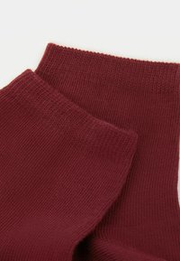 Calzini in cotone bordeaux con texture a coste e polsini elasticizzati. Presentano una finitura liscia e un colore uniforme su tutta la superficie.