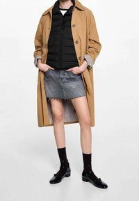 Beige trenchcoat, svart vadderad väst, grå denimkjol, svarta ankelsockor och svarta Mary Jane-skor. Har knappar och fickdetaljer.