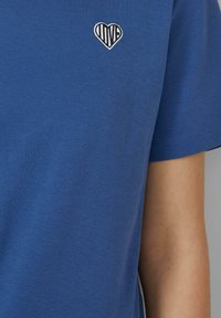 Blauw katoenen t-shirt met een ronde halslijn en korte mouwen, voorzien van een witte geborduurde hartafbeelding met het woord "LIEFDE."