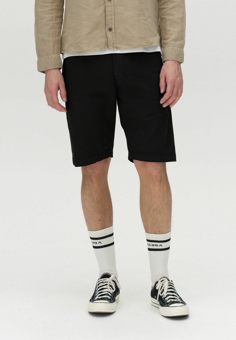 Schwarze Baumwollshorts im geraden Schnitt, kombiniert mit weißen knielangen Socken mit schwarzen Streifen und schwarzen Turnschuhen.