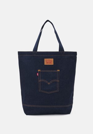 Dunkelblaue Denim-Tasche mit zwei Griffen, sichtbaren Nähten und einer Vordertasche mit einem klassischen Logo-Patch.