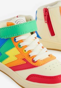 Tenisice visoke forme u krem boji, s raznobojnim naglascima plave, zelene, narančaste, žute i crvene boje. Bijele vezice i crni zatvarač na peti.