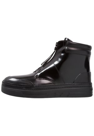 Błyszczący czarny sneaker za kostkę z przednim zamkiem błyskawicznym, grubą gumową podeszwą i wyściełanym kołnierzem wokół kostki, pokazany w profilu bocznym.