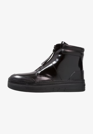 Zapatilla deportiva de caña alta negra y brillante con cremallera frontal, suela gruesa de goma y cuello acolchado alrededor del tobillo, mostrada de perfil.