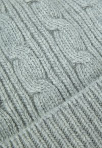 Tessuto lavorato a maglia grigio chiaro con motivi a treccia in rilievo e texture a costine. Il filato appare morbido e accogliente, ideale per mantenere il calore.