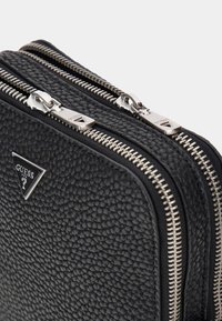 Schwarze Leder-Doppeltasche mit strukturiertem Oberflächenmaterial, dualen silbernen Reißverschlüssen und einem dreieckigen Logopiktogramm.
