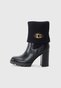 Black leather ankle boot with ribbed knit upper, featuring a round gold logo accent and a chunky high heel with a rugged sole.