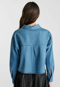 Korte denim shirt in lichtblauw, met een klassieke kraag, knoopmanchetten en versieringen van kleine zilveren studs op de rug.