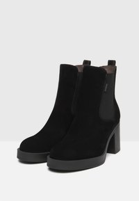 Stivali alla caviglia in suede nero con tacco impilato, pannelli laterali elasticizzati e linguette per una facile indossabilità. Texture liscia e design con punta arrotondata.