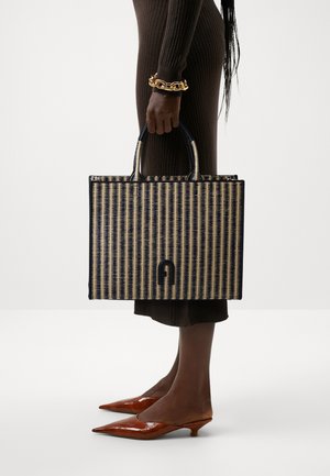 Sac fourre-tout rectangulaire avec un design tressé en bleu marine et beige, doté de poignées robustes et d'un accent logo distinctif au centre.
