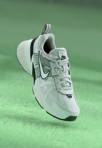 Nike tossud, millel on valge sissetõmmatav pealis, mustad aktsendid, silmatorkav swooshi logo, massiivne tald ja tekstuuriga detailid külgedel.