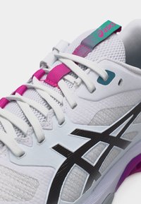 Λευκό αθλητικό παπούτσι Asics με μαύρο λογότυπο, λευκά κορδόνια και ροζ και τιρκουάζ λεπτομέρειες στη γλώσσα και τους βρόχους των κορδονιών.