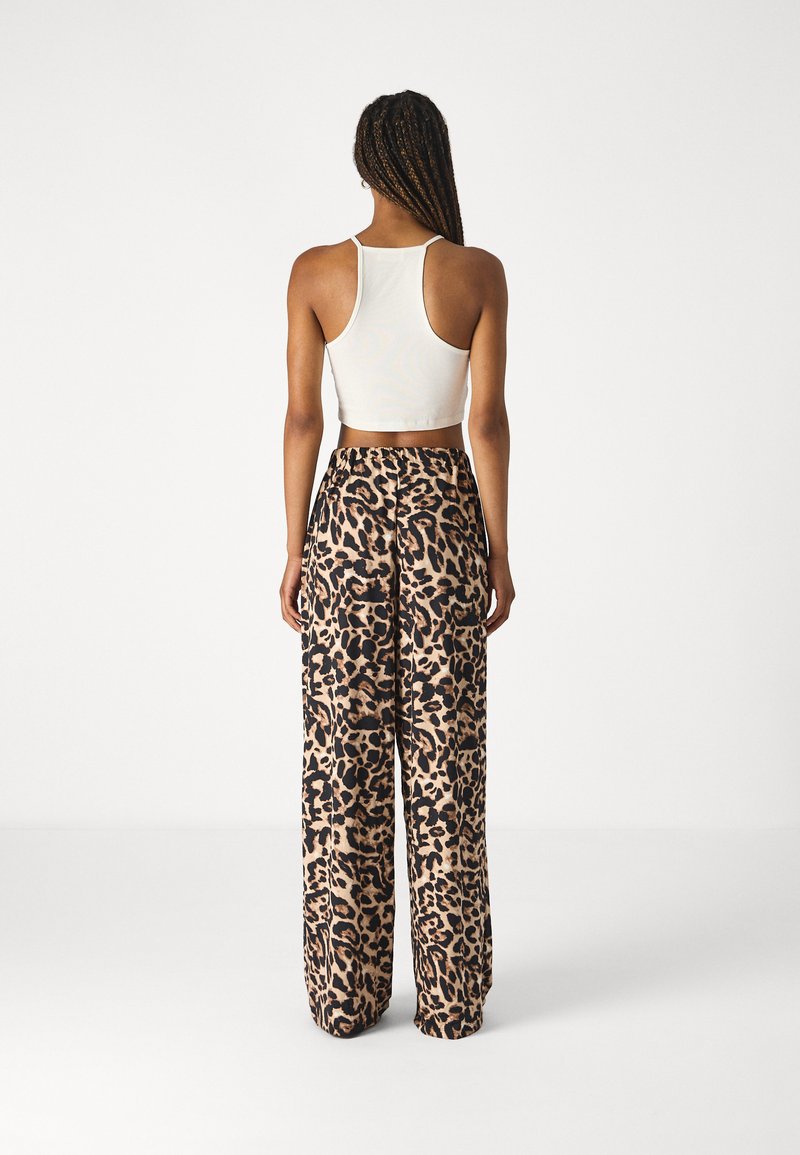 Un débardeur blanc court associé à un pantalon loose à imprimé léopard présentant un motif beige et noir. Tissu doux, ceinture élastique, coupe décontractée.