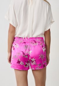 Roze satijnen shorts met een smocktail, voorzien van een levendig bloemenpatroon in wit en paars. Gladde textuur en ontspannen pasvorm.
