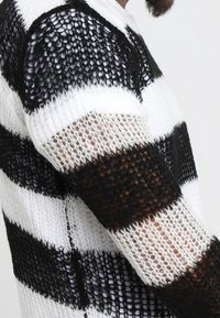 Maglione a righe bianche e nere, realizzato in maglia con una texture larga e aperta e maniche corte. Presenta ampie righe orizzontali.