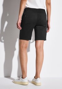 Černé džínové šortky s přímým střihem, zadními kapsami a prošitými detaily, doplněné bílými teniskami. Látka vypadá hladká a odolná.