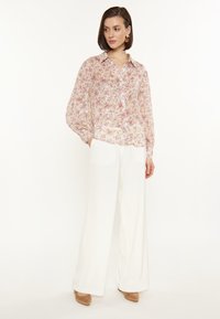 Bloemenblouse met een lichtroze achtergrond, losse fit, knoopsluiting en glanzende accenten; gecombineerd met witte wijde broek en beige hakken.