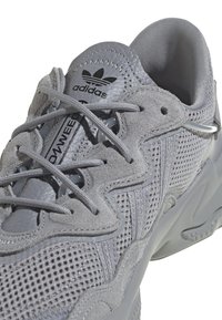 Scarpe da ginnastica grigie realizzate con un mix di materiali in suede e mesh, superfici testurizzate, lacci prominenti e il logo adidas sulla linguetta.