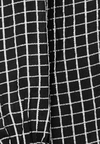 Tessuto nero con un motivo a griglia bianca, caratterizzato da forme quadrate uniformi. Il materiale ha una finitura texturizzata con cuciture visibili.