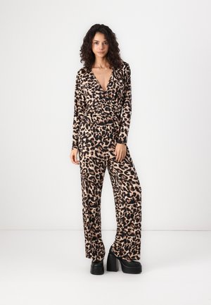 Mono de estampado de leopardo en taupe y negro, con un escote en V profundo, mangas largas y piernas anchas. Lleva tacones de plataforma negros y gruesos.