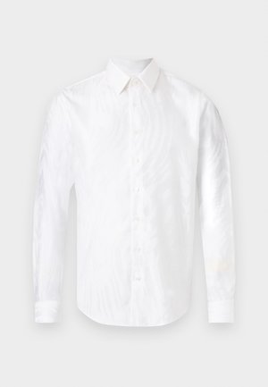 Bílá košile s dlouhým rukávem a zapínáním na knoflíky, s špičatým límečkem, položena na světle pozadí.