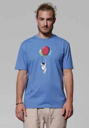 Blauwe katoenen t-shirt met een astronaut-figuur die rode, groene en blauwe ballonnen vasthoudt. Korte mouwen en een ronde hals.