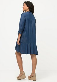 Denimmekko, jossa on kolme neljännesosahihnaa ja röyhelöhelma; hihansuissa on ryppytty yksityiskohta; tummansinisessä värissä, kevyttä materiaalia.