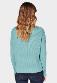Pull en maille côtelée de couleur bleu sarcelle clair, avec une coupe décontractée, des manches longues et une texture subtile, doté d'un ourlet arrondi et sans pièces métalliques visibles.