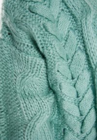 Svetlo mint zelena pletenina z vzorcem kablov, z teksturirano, mehko površino in udobnim, debelim občutkom.