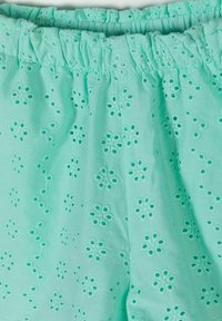 Tissu turquoise clair avec motif floral en broderie ajourée et ceinture élastique froncée.