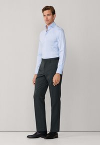  lichtblauw overhemd met lange mouwen en knoopsluiting, voorzien van een puntige kraag, gecombineerd met donkergrijze op maat gemaakte broek en zwarte leren schoenen.