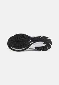 Suela de zapato deportivo negro con surcos, estrías y un acento blanco. Presenta un diseño resistente con goma texturizada para mayor tracción.