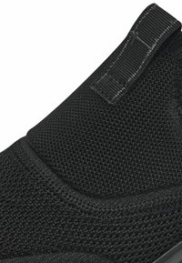 Primo piano di una scarpa slip-on nera lavorata a maglia con linguetta e cuciture a contrasto nell'area superiore del tallone.