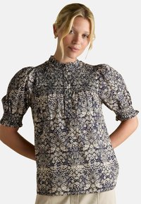 Ziedu apdrukas blūze ar augstu kakla izgriezumu, pūkainām piedurknēm un smalku virsotni, kas ir tumši zila ar krēmkrāsas akcentiem; viegla auduma.